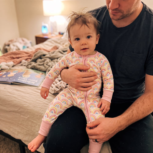 Dad holding his baby wearing the Sweet Sleep Pastel Rainbows Zippy footie