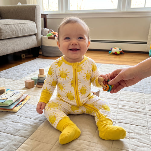 Smiling baby playing on a rug in Sweet Sleep Sunshine Zippy footie pajamas