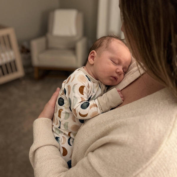 Sleeping baby held on a shoulder in the Luna Neutral Zippy footie
