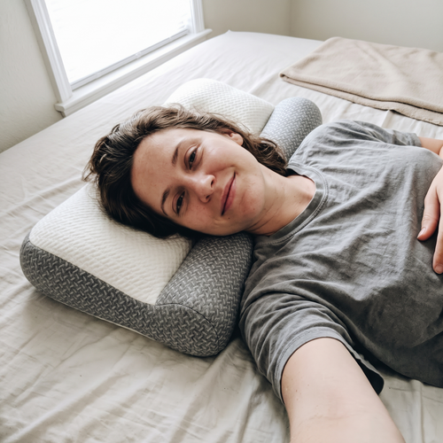 Woman lying on a bed with her head on a Sweet Sleep Cervical Contour Pillow